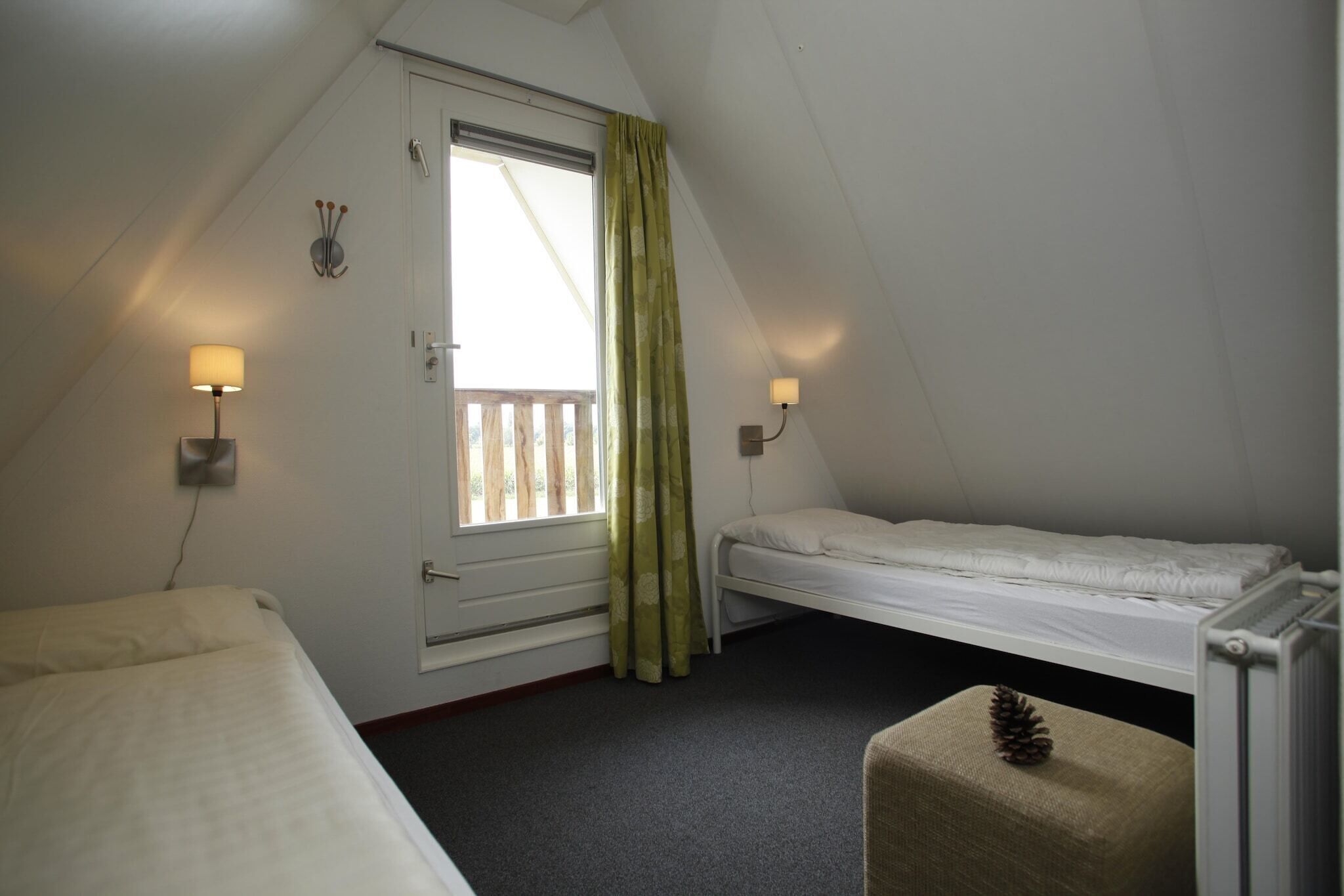 Een kleine, driehoekige kamer met twee bedden, een raam met gordijnen en twee wandlampen.