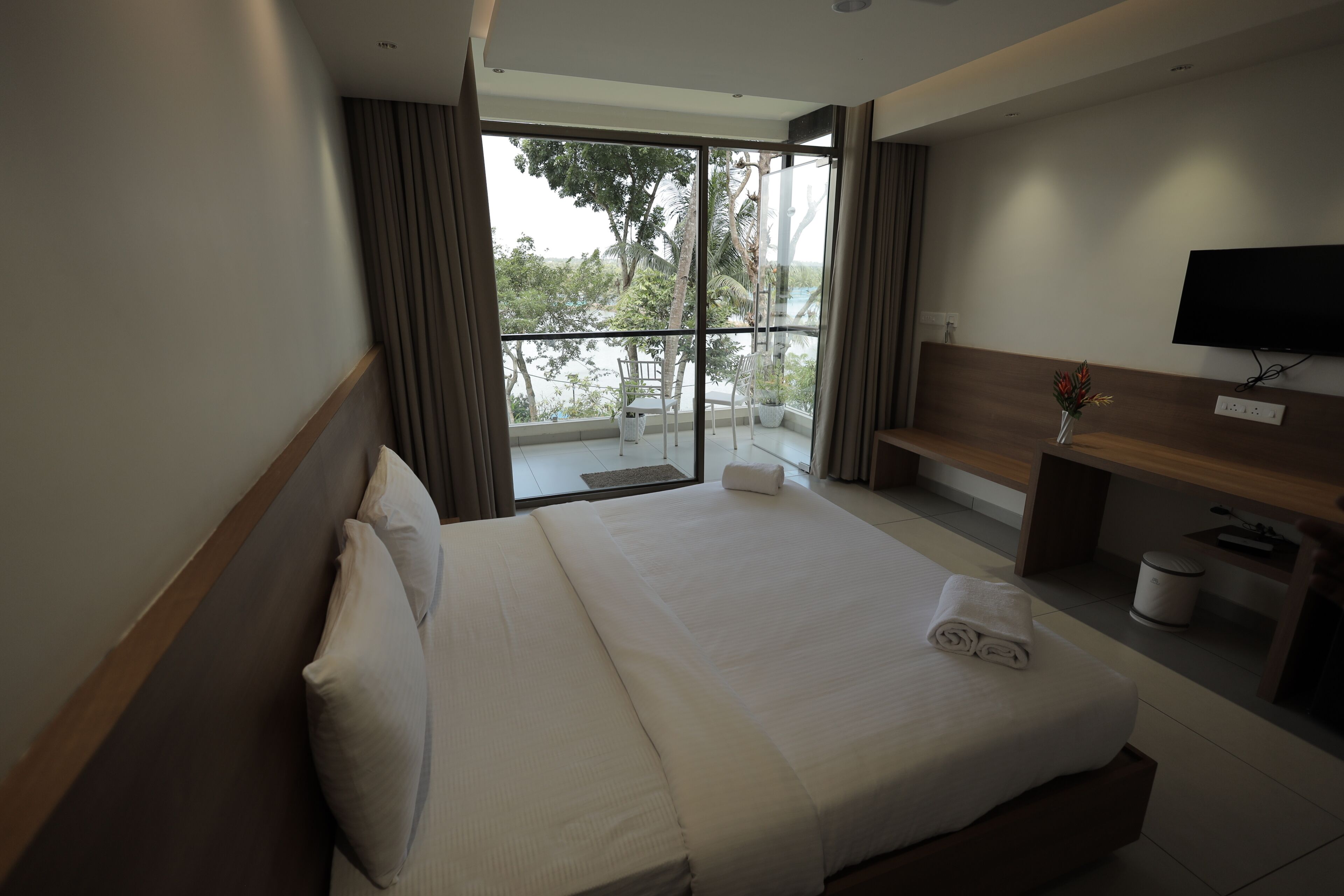 A hotel room with a bed, a television, a desk, and a view of the outdoors.