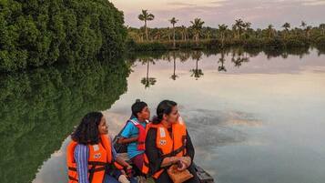 A group of people in a boat on a calm body of water with dense greenery on one side.