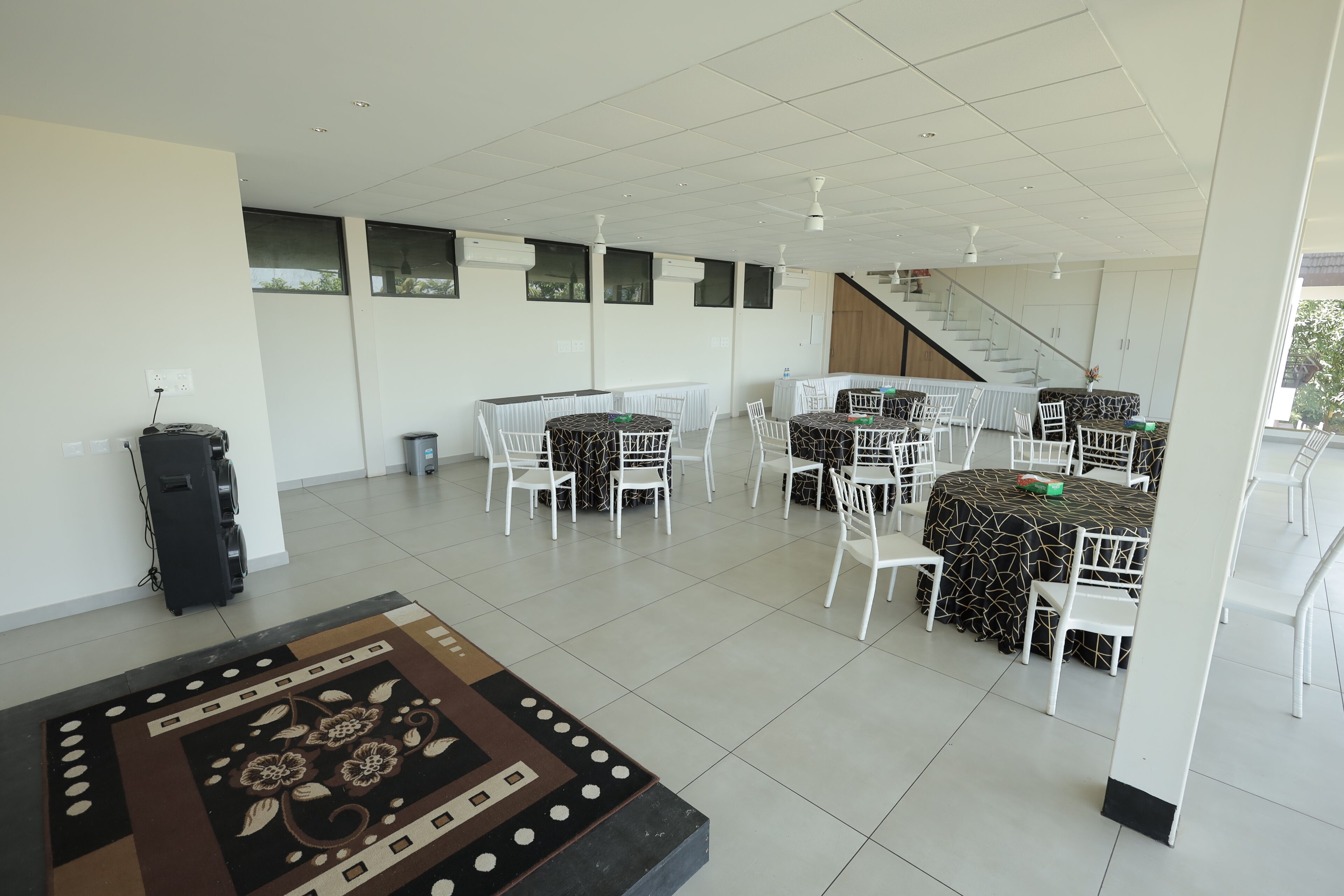 A spacious indoor area with multiple tables and chairs, a staircase, and a patterned rug.