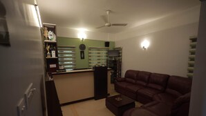 Een woonkamer met een bruine leren bank, een salontafel, een receptiebalie en een plafondventilator.