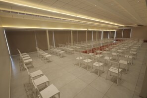 A large, empty conference room with rows of white chairs and tables, a red carpet, and a high ceiling with recessed lighting. - The Brook Serene – A Nature Themed Boutique Resort, Kollam (Kollam)