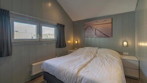 A bedroom with a large bed, two bedside tables, a window with curtains, a radiator, and a wall-mounted picture. - Beach house 't Koepeltje near dunes (Groote Keeten)