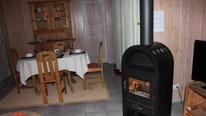 A dining area with a table set for four, a black wood-burning stove, and a wooden cabinet in the background. - Ferienhaus mit Sauna im Ferienpark Mirow (Granzow)