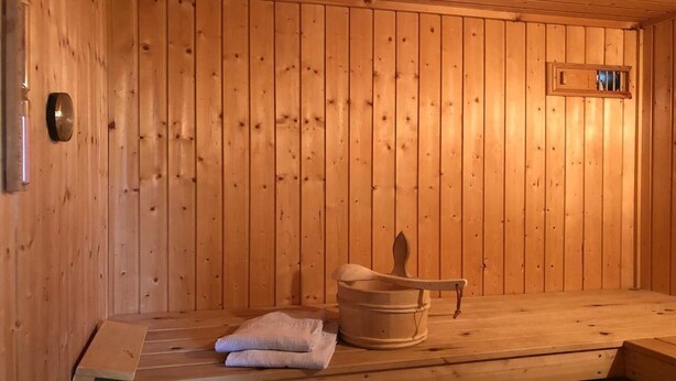 A wooden sauna with a bench, a wooden bucket, and a towel. - Ferienhaus mit Sauna im Ferienpark Mirow (Granzow)