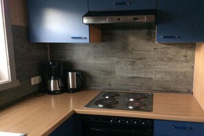 Une cuisine avec des meubles bleus, une hotte de cuisinière en acier inoxydable, une machine à café et une cuisinière à gaz.