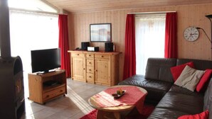 A living room with a television, wooden cabinets, a sofa, and a red rug. - Ferienhaus mit Sauna im Ferienpark Mirow (Granzow)