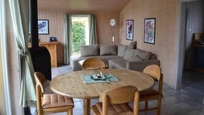 Une pièce chaleureuse avec un plafond en bois, une table ronde en bois entourée de chaises, un canapé avec des coussins et une fenêtre avec des rideaux.