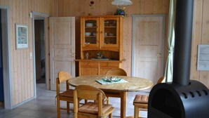 Een kamer met houten lambrisering, een ronde eettafel, stoelen, een kast met glazen deuren en een houtkachel.