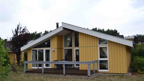 Un bâtiment jaune avec un toit en pente, de grandes fenêtres et un porche couvert avec des chaises.