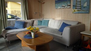 A cozy living room with a beige sofa, blue cushions, a wooden coffee table with flowers, and two paintings on the wall.