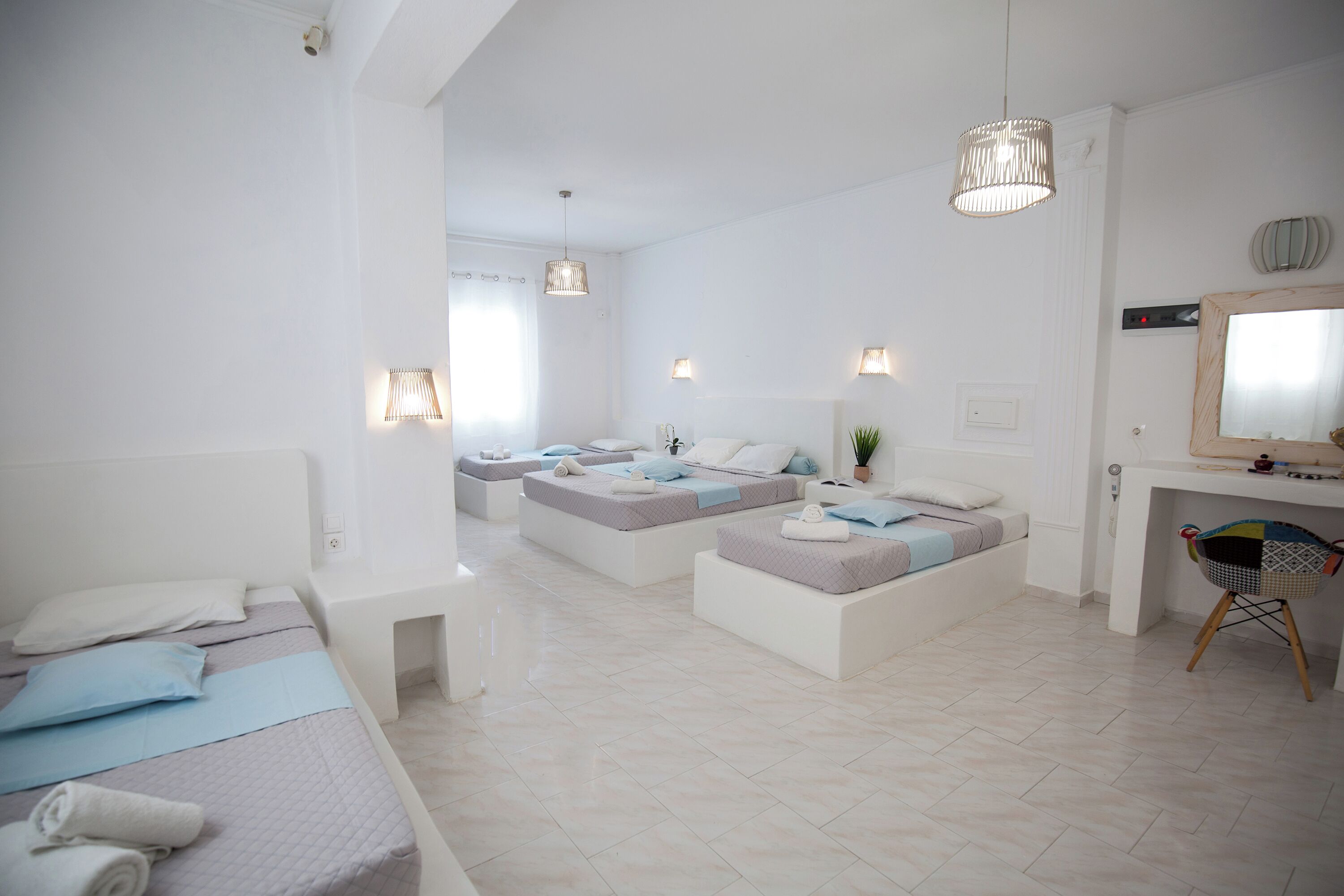 Une chambre moderne et bien éclairée, dotée d’un grand lit, de deux petits lits et d’un espace bureau avec une chaise.