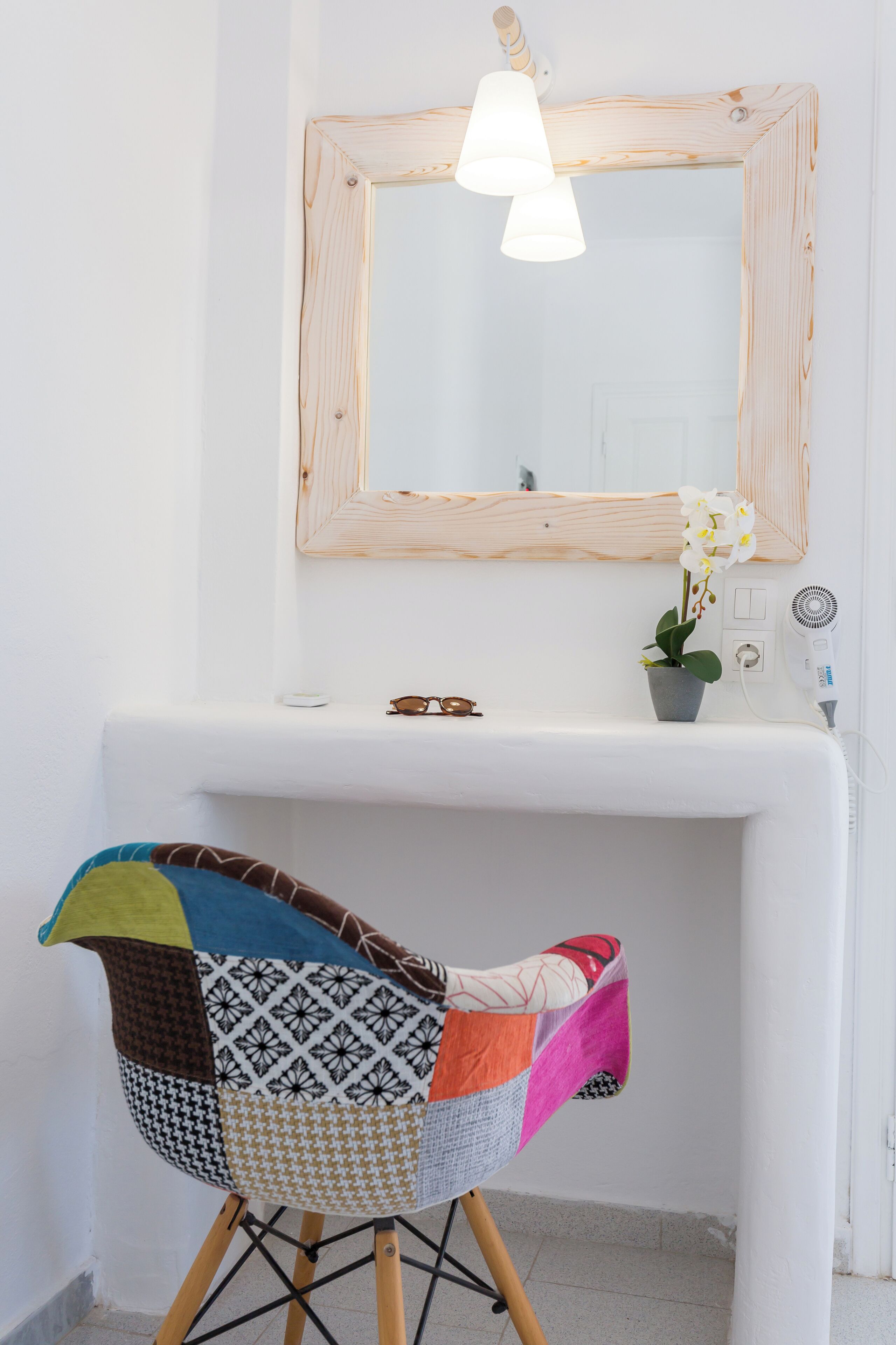 A bathroom with a white sink, a mirror, a hanging light fixture, a potted orchid, and a colorful chair.
