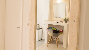 A hallway with a wooden-framed mirror reflecting a bathroom with a sink, a small stool, and a potted plant. - Blue Island Hotel (Santorini)
