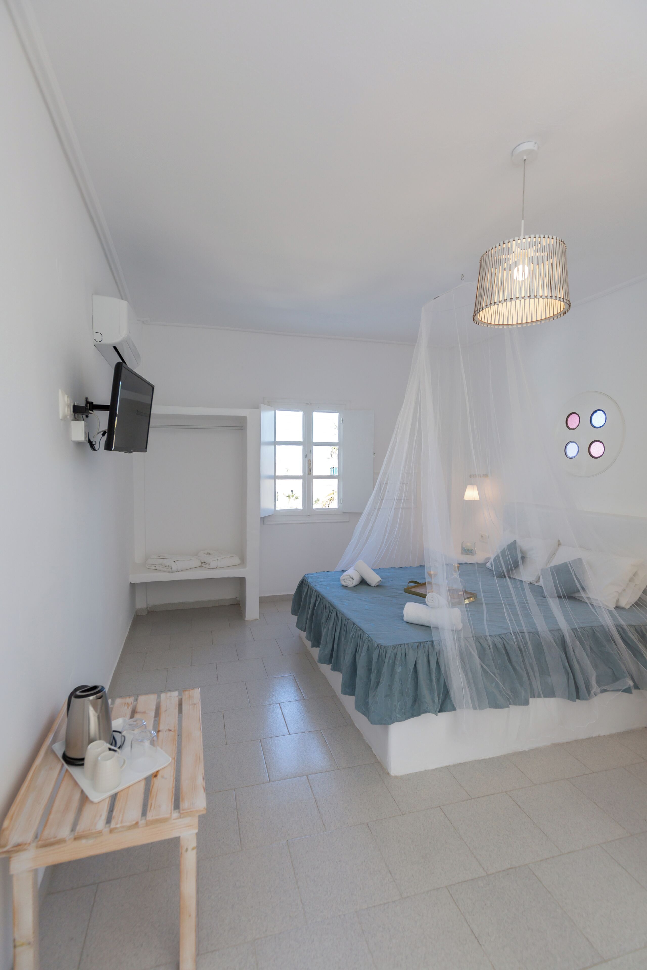 A bedroom with a bed, bedside table, TV, and a window.