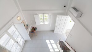 A spacious room with a high ceiling, a large window, and a door leading outside. - Blue Island Hotel (Santorini)