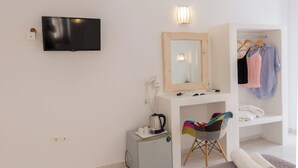 A modern, minimalist room with a flat-screen TV, a mirror, a small kitchenette, and a walk-in closet. - Blue Island Hotel (Santorini)