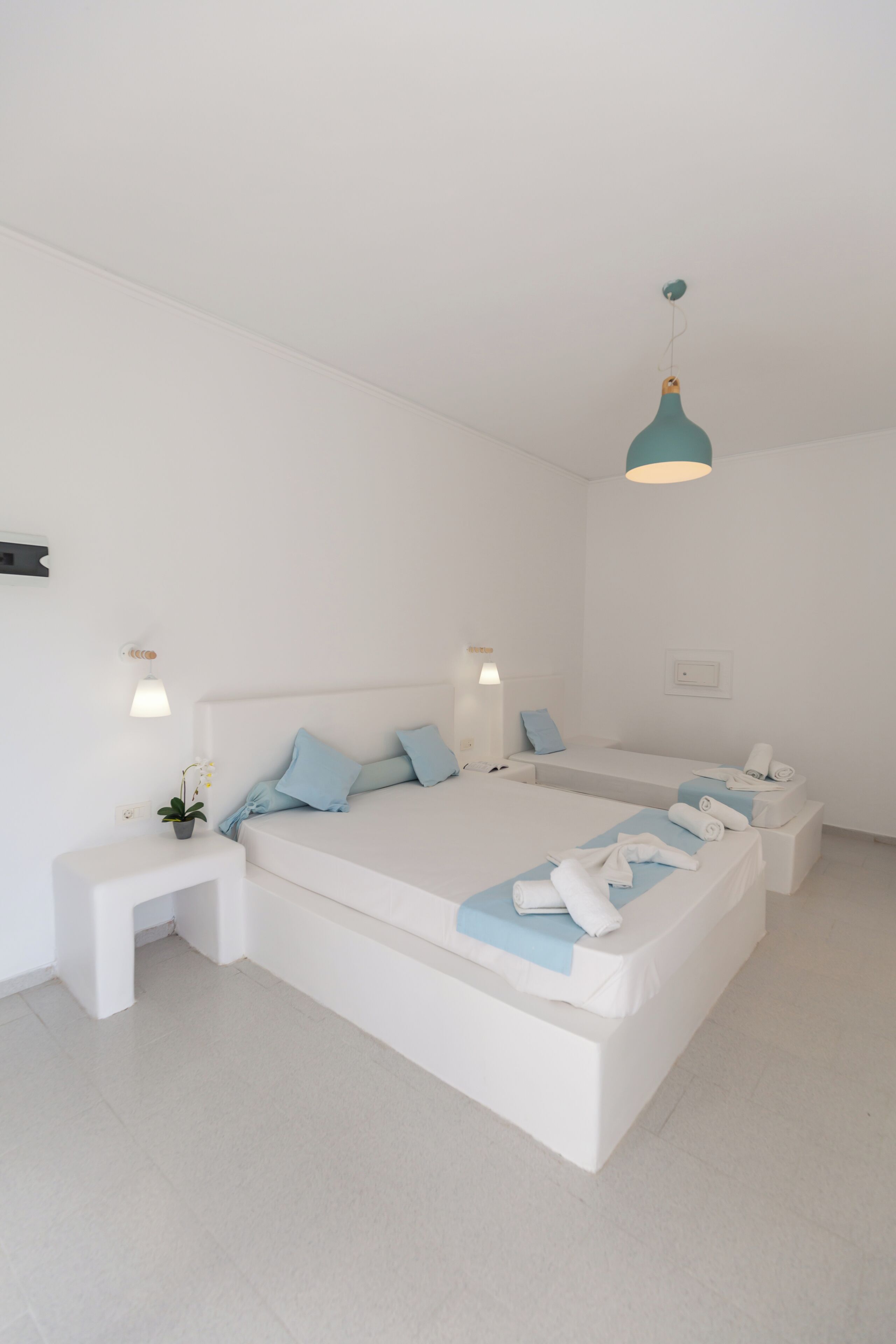 A modern, minimalist bedroom with a large bed, bedside tables, and a hanging light fixture.