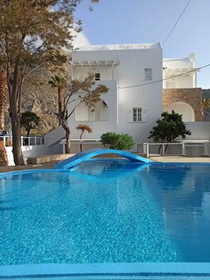 A clear swimming pool with a blue arch bridge, surrounded by white buildings and trees. - Blue Island Hotel (Santorini)