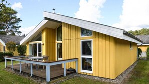 Une maison jaune avec une terrasse, de grandes fenêtres et un toit blanc.