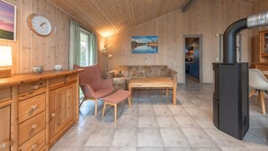 Un intérieur en bois comprenant un canapé, un fauteuil, une table, une horloge et un coin cuisine.