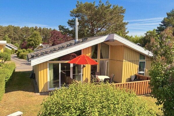 Een klein houten huisje met schuin dak, een glazen deur en een rode paraplu.