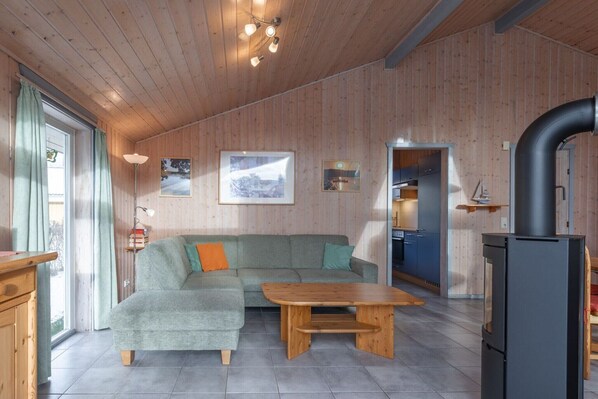 Een gezellige woonkamer met een hoekbank, een houten salontafel en een keuken die zichtbaar is door een open deur.