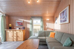 Una habitación acogedora con techo de madera, un sofá con cojines, una mesa de madera, un mueble con cajones y una ventana con cortinas.