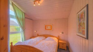 A wooden-paneled bedroom with a single bed, a nightstand, a window with curtains, and a framed picture on the wall.