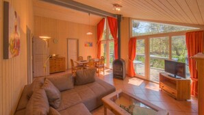 Un salón acogedor con sofá, televisor, chimenea y ventanas amplias.