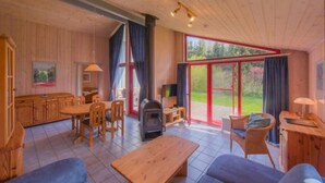 A spacious living area with a wooden floor, a fireplace, a dining table, and a large sliding glass door leading to a garden. - Ferienhaus mit Sauna im Ferienpark Mirow (Granzow)