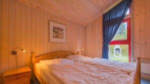 Ein gemütlicher Holzraum mit einem Bett, einem Nachttisch und einem Fenster mit Vorhängen.