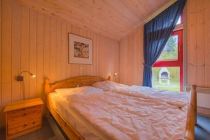 Acogedora habitación de madera con una cama, una mesita de noche y un ventanal con cortinas.