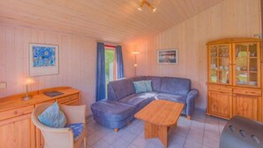 A cozy room with a wooden ceiling, a blue sofa, a wooden table, a wicker chair, and a cabinet with glass doors. - Ferienhaus mit Sauna im Ferienpark Mirow (Granzow)