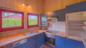 A compact kitchen with wooden walls, a built-in oven, a microwave, and a refrigerator. - Ferienhaus mit Sauna im Ferienpark Mirow (Granzow)