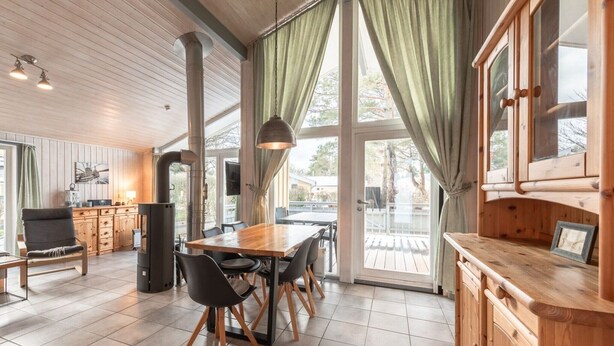 A modern kitchen with a wooden table, chairs, and a large window with curtains. - Ferienhaus mit Sauna im Ferienpark Mirow (Granzow)