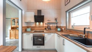 A modern kitchen with wooden cabinets, a built-in oven, a sink, and a window providing natural light. - Ferienhaus mit Sauna im Ferienpark Mirow (Granzow)