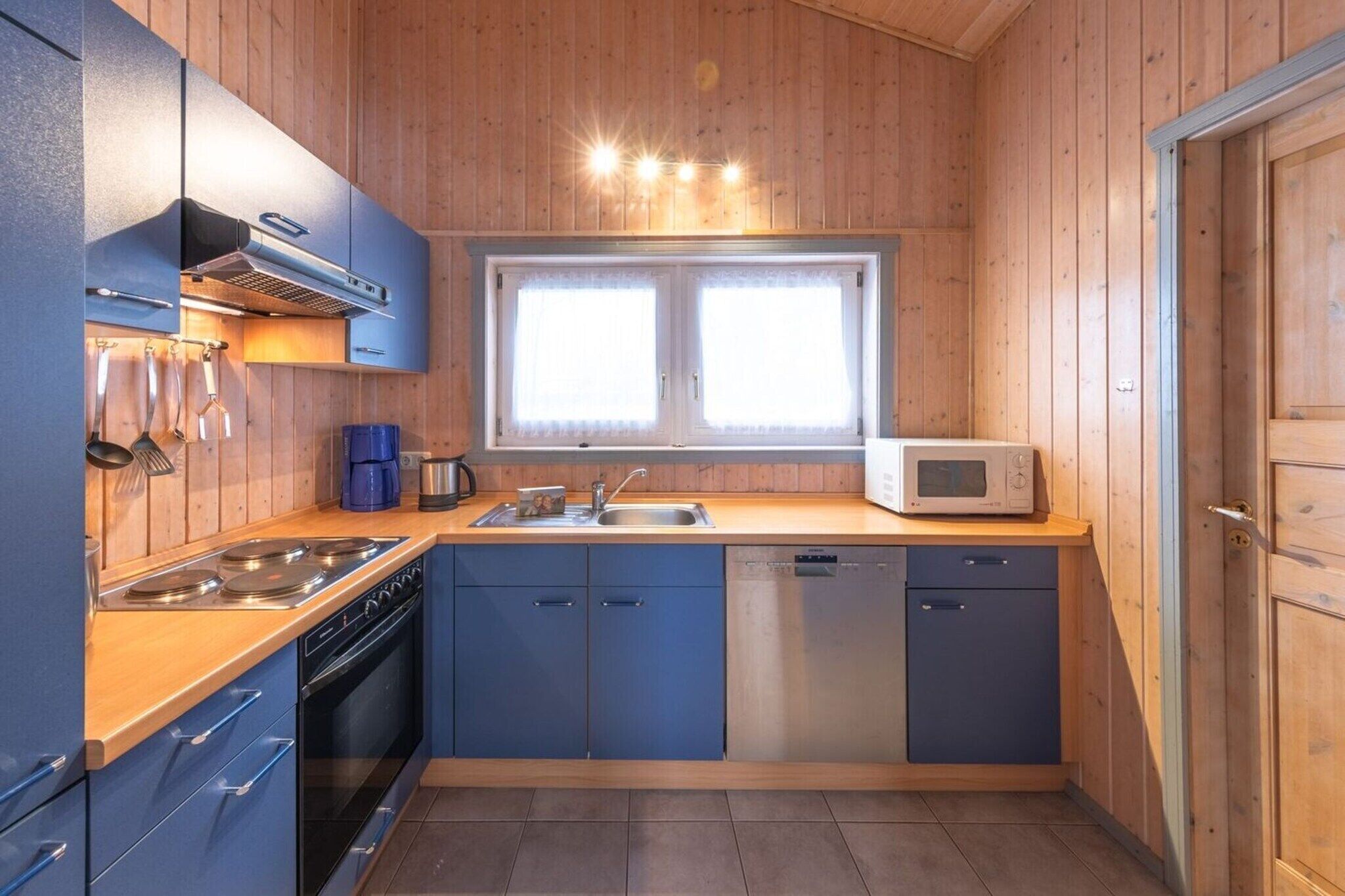A compact kitchen with wooden walls, a stainless steel stove, a microwave, and a dishwasher.