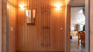 Un couloir aux murs lambrissés, agrémenté d’un miroir et de patères, qui mène à une cuisine avec des meubles en bois et une table à manger.
