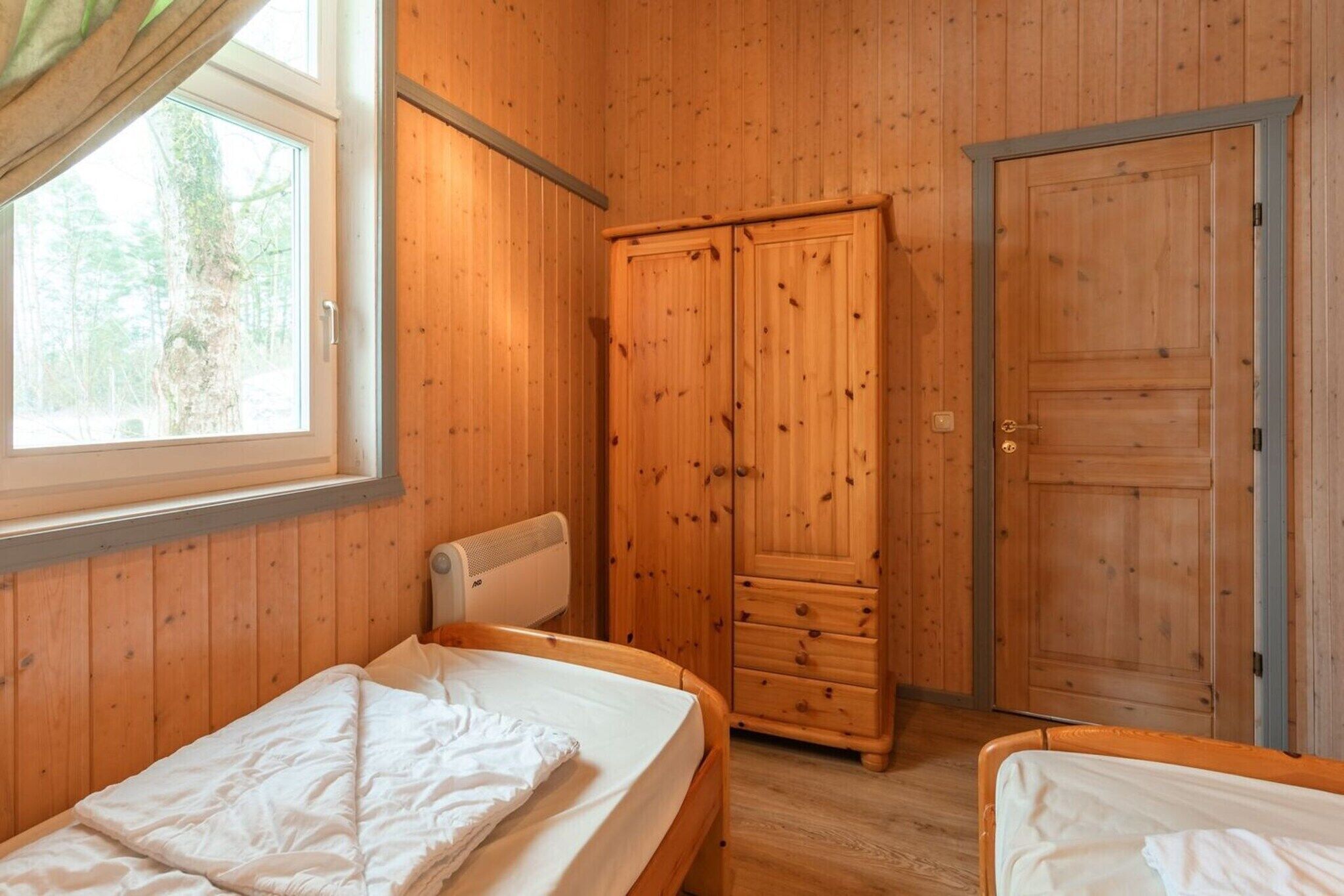 A wooden room with two beds, a wardrobe, and a window with a view of trees.