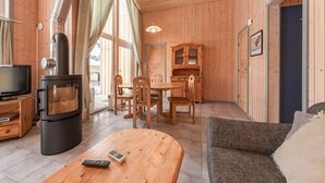 Un salon chaleureux avec un poêle à bois, une télévision, un coin repas avec des chaises et une table, et un canapé.