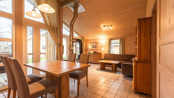 A wooden interior with a dining table, chairs, a sofa, and a kitchen area. - Ferienhaus mit Sauna im Ferienpark Mirow (Granzow)