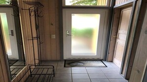 Ein schmales Entree mit einer Tür zu einem Zimmer, einem Metallregal und einem gefliesten Boden.