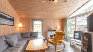 Une pièce chaleureuse avec un plafond en bois, un canapé, un fauteuil à bascule, une table en bois et un téléviseur.