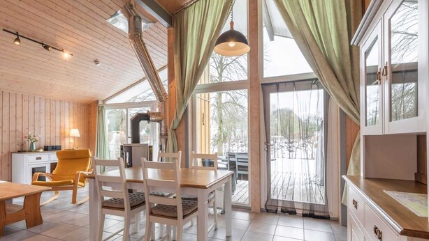 L’intérieur chaleureux d’un chalet avec un coin repas, des murs en bois, de grandes fenêtres et une vue sur le paysage enneigé.