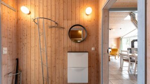 Une salle de bain aux murs lambrissés, équipée d’une douche, d’un miroir et d’un meuble blanc.