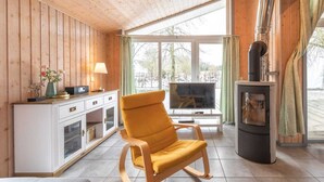 Une pièce chaleureuse avec des murs en bois, une armoire blanche, une chaise jaune, une cheminée et une grande fenêtre.