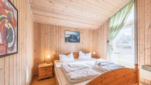 Une chambre aux murs lambrissés, avec un lit, des tables de chevet et une fenêtre avec des rideaux.