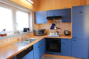 A compact kitchen with blue cabinets, a microwave, a dishwasher, and a window with curtains.