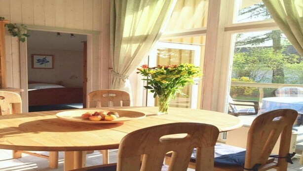 Ein Holzespeisesaal mit Stühlen, einer Vase mit Blumen und Blick ins Freie durch große Fenster.